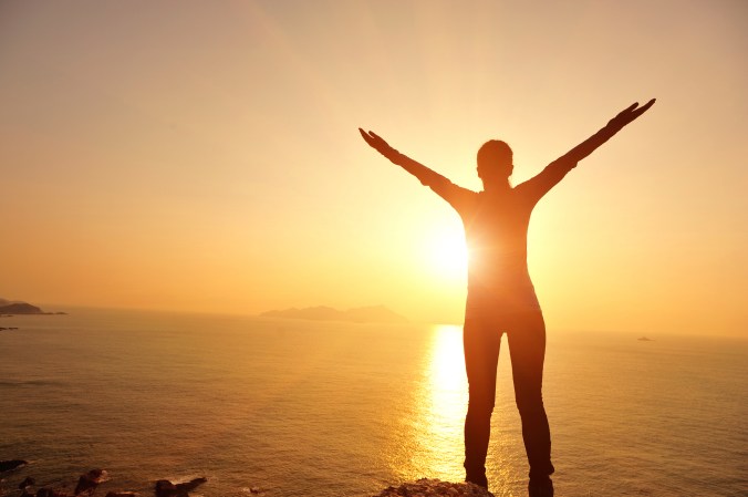 WomanCheeringInSunshineOnCliffOverOcean